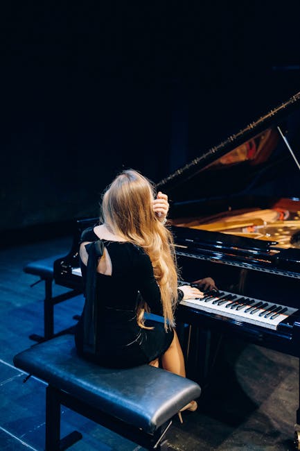 A female musician playing the piano on stage, captured in an elegant pose from behind.