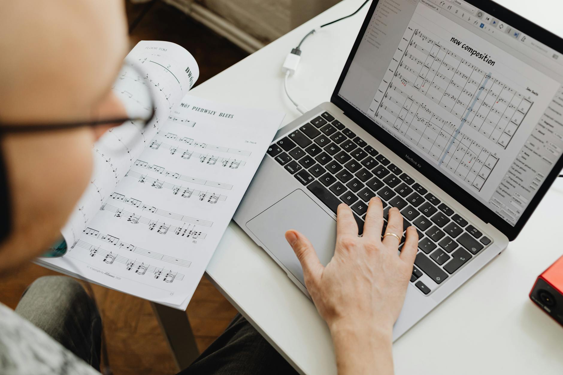 A musician using a laptop to compose music with music sheets nearby. Creative workspace.